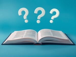 faq-insolvencia-colombia.jpg » Montenegro Asociados » Montenegro Asociados Open book on a blue background with three white question marks floating above, suggesting questions or learning.